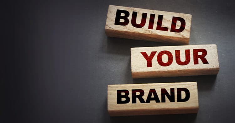 Three wooden blocks stacked diagonally, each with bold text saying "BUILD YOUR BRAND" on a dark background.