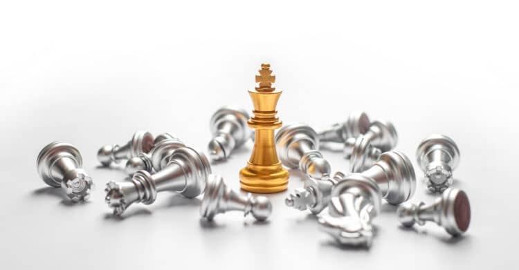 A gold chess king stands upright at the center of a white surface, surrounded by silver chess pieces that have fallen on their sides. The image visually represents leadership and strategy, making it relevant for content about how to Improve Your Brand and stand out from competitors.