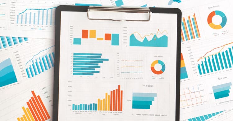 A clipboard displays multiple colorful charts and graphs showing sales trends, totals, and percentages, placed on top of scattered analytics reports. The image supports content about data driven decisions and performance tracking to Improve Your Brand and guide strategic growth.