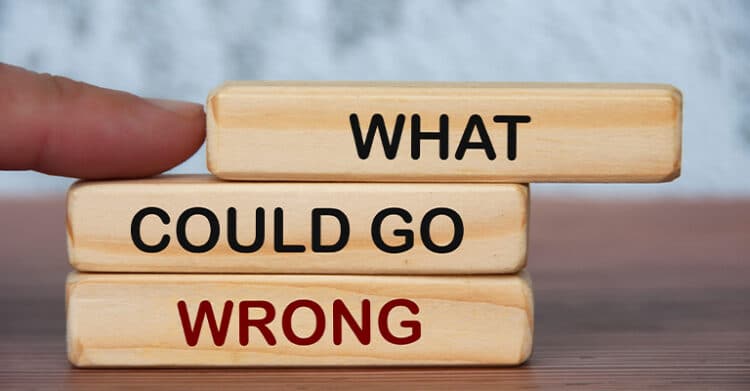 How Does Keyword Length Impact SEO Ranking? 8 Three wooden blocks stacked on a table display the phrase "WHAT COULD GO WRONG" in bold letters, with the word "WRONG" highlighted in red. A person's finger is about to push the top block, suggesting risk, uncertainty, or potential failure.