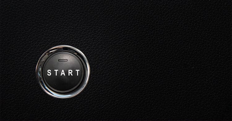 A close-up of a black car push-to-start button with the word “START” in white capital letters, set against a textured black dashboard. The image represents beginning a journey, launching something new, or initiating action.