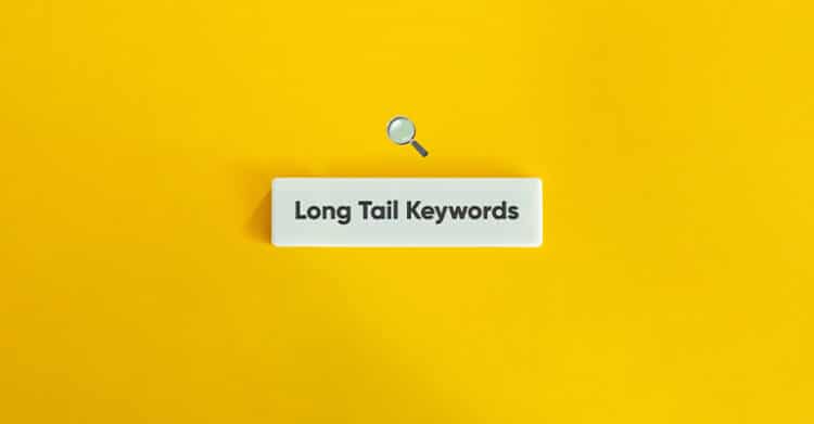 A white search bar with the words "Long Tail Keywords" in bold sits centered on a bright yellow background, with a small magnifying glass icon above it. The image visually emphasizes the concept of targeting specific, low-competition keyword phrases in SEO strategy.