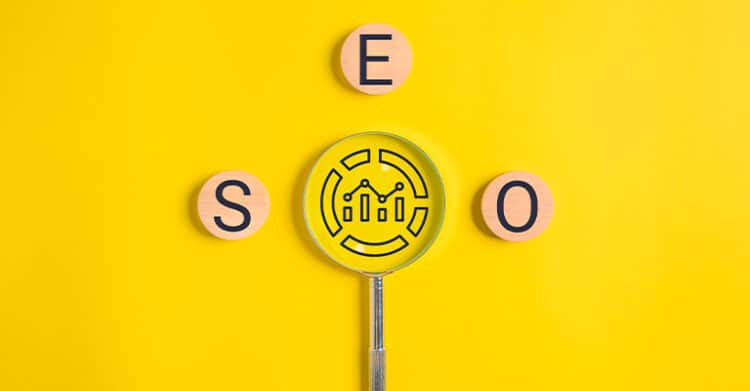 Three wooden circles with the letters S, E, and O are arranged on a bright yellow background, with a magnifying glass highlighting a data analytics icon in the center. The image creatively represents SEO and the role of analytics in search engine optimization.