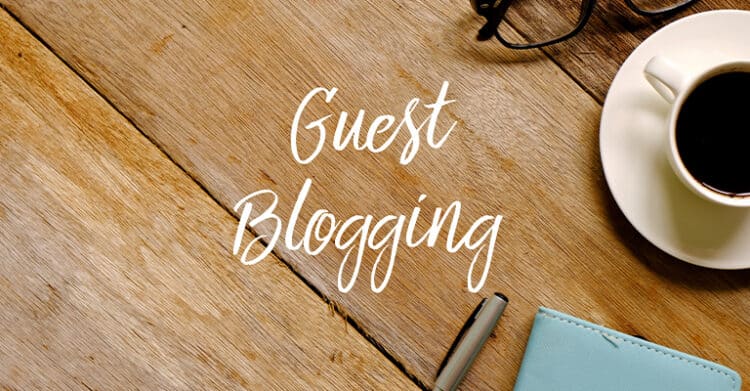 A flat lay photo on a wooden table features the words "Guest Blogging" in elegant script, surrounded by a cup of coffee, eyeglasses, a pen, and a light blue notebook. The image symbolizes content creation and collaboration in digital marketing through writing blog posts for other websites.