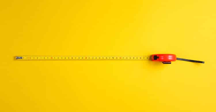 Personal Branding Strategy: Build a Brand That Opens Doors 10 A yellow measuring tape extended horizontally across a bright yellow background with a red tape measure casing on the right. The image represents measurement, accuracy, planning, or tracking length or progress in a simple and visually bold way.