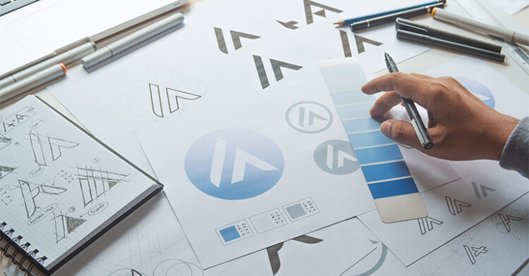 Designer working on logo concepts with sketches, color palettes, and design tools on a desk.