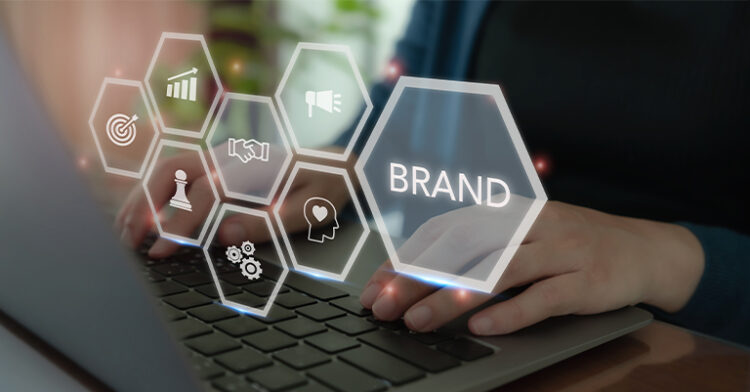 Hands typing on a laptop with digital hexagonal icons displaying "Brand" and related concepts like strategy, marketing, and goals.