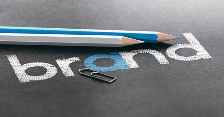 The word "brand" partially sketched on a black surface with two pencils and a paperclip beside it.