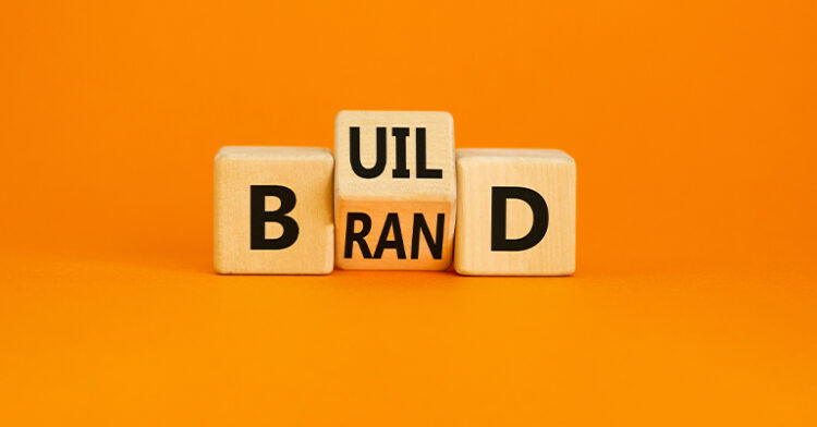 Wooden blocks spelling out "BUILD BRAND" against a bright orange background.