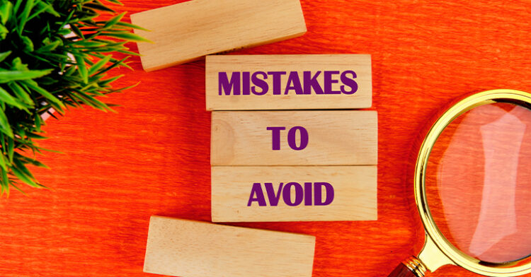 Wooden blocks with the phrase "MISTAKES TO AVOID" written in purple, placed on an orange surface next to a magnifying glass and green leaves.