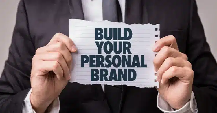 How to Develop a Personal Brand that Resonates 3 A person in a suit holding a torn notebook page with the bold text “BUILD YOUR PERSONAL BRAND” printed on it.