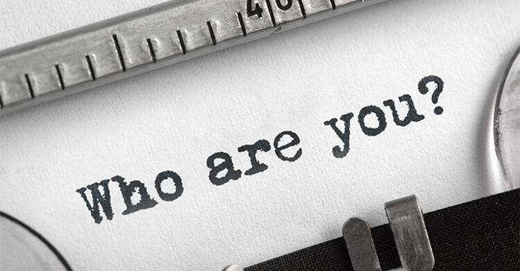 Close-up of a typewriter printing the words "Who are you?" on white paper.