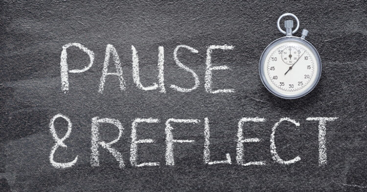A chalkboard with the words "Pause & Reflect" written in white chalk, accompanied by a stopwatch showing a time measurement.