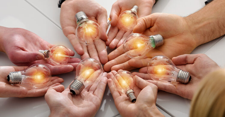 Multiple hands holding glowing light bulbs, symbolizing teamwork, collaboration, and shared ideas.