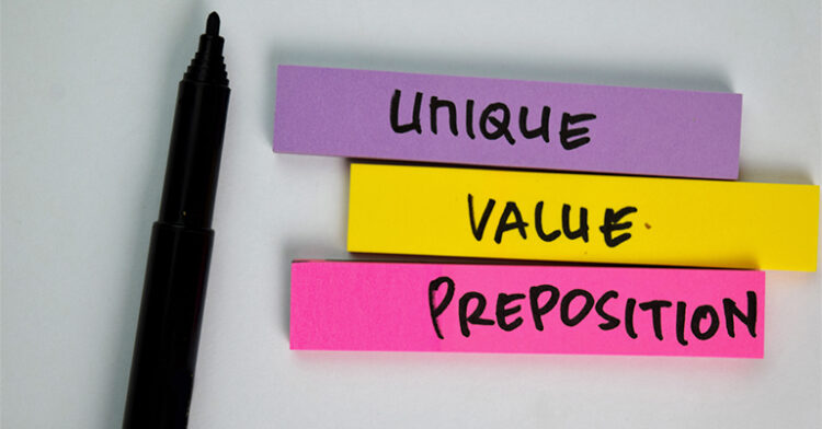 Purple, yellow, and pink sticky notes stacked on a white surface, reading “Unique Value Preposition” with a black marker nearby. The word “Preposition” is a misspelling of “Proposition.”