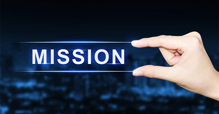 Human fingers pinching a glowing strip displaying the word “MISSION” in white capital letters, with a blurred dark background.