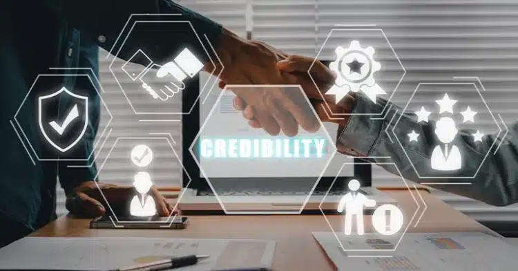 Two people shaking hands over a desk with the word "Credibility" on a screen and trust-related icons overlayed.