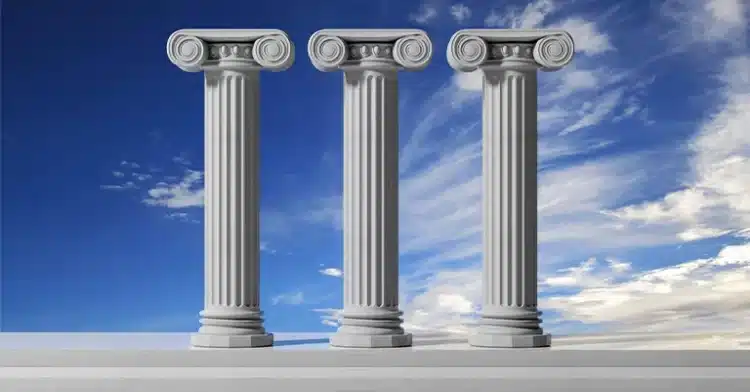 Three classical Ionic columns standing against a vibrant blue sky with wispy clouds.
