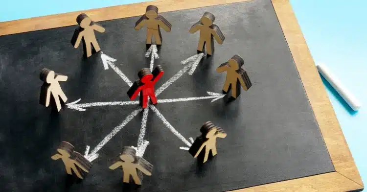 Red wooden figure in the center of a chalkboard with arrows pointing to surrounding brown figures, symbolizing leadership or influence.