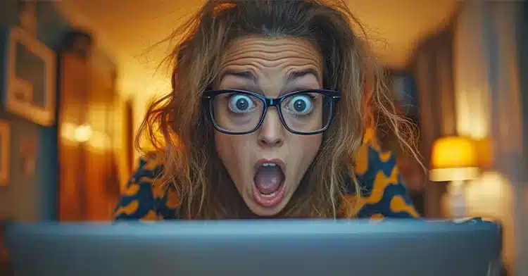 How to Manage Your Online Identity: The Ultimate Guide 5 Shocked woman with glasses staring at a laptop screen with wide eyes and open mouth in a dimly lit room.