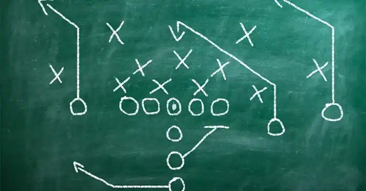 Football play strategy drawn in white chalk on a green chalkboard with Xs, Os, and directional arrows.