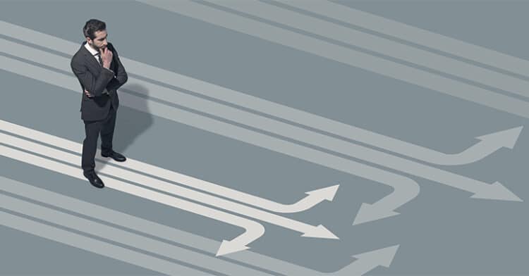 Businessman standing thoughtfully among several diverging arrows on the ground, symbolizing decision-making, strategy, and choosing direction.