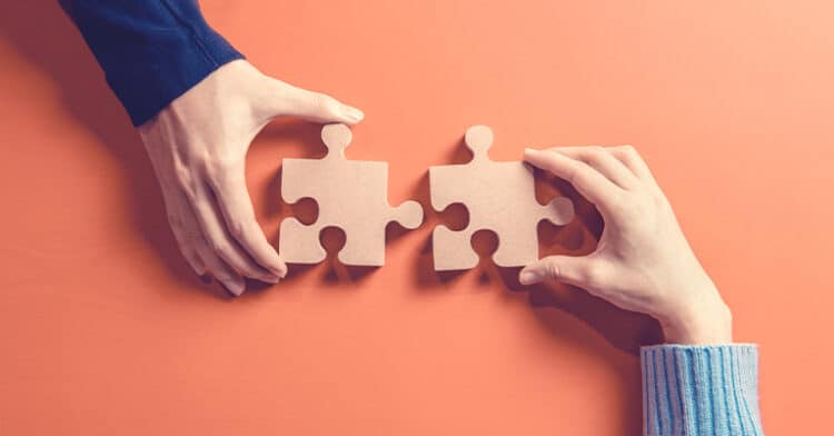 Two hands connecting puzzle pieces on an orange background, symbolizing partnership and strategic influencer collaboration.