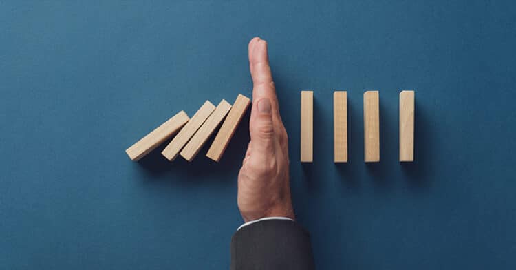 A hand stopping a row of falling dominoes on a blue background, symbolizing intervention or prevention of a chain reaction.