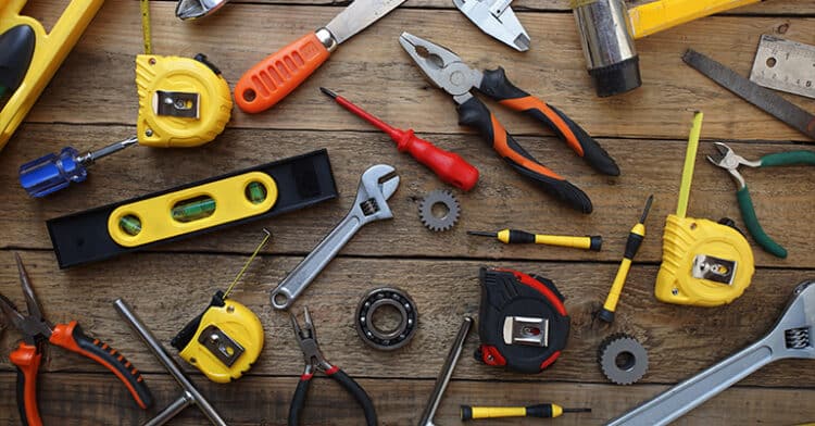 Assorted hand tools including wrenches, tape measures, pliers, and screwdrivers arranged on a wooden surface.