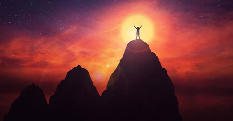 A person stands triumphantly on a mountain peak during sunset, silhouetted against a glowing sky, representing achievement, success, or reaching goals.