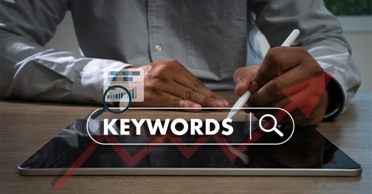 Person using a stylus on a tablet with the word “KEYWORDS” and search icon overlay, representing keyword research and search engine strategy.