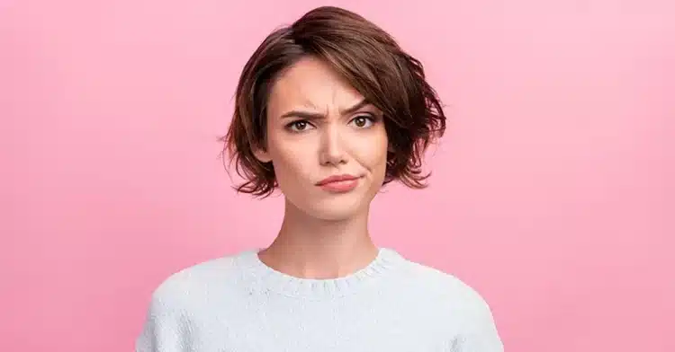 How to Use Social Media Influencers to Improve Your Marketing 5 Woman with short brown hair raising one eyebrow and looking skeptical against a solid pink background.