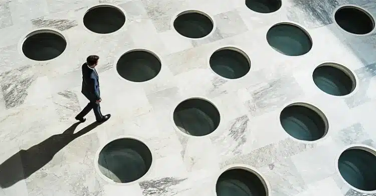 Businessman walking carefully across a floor with multiple circular holes, representing risk and strategy.