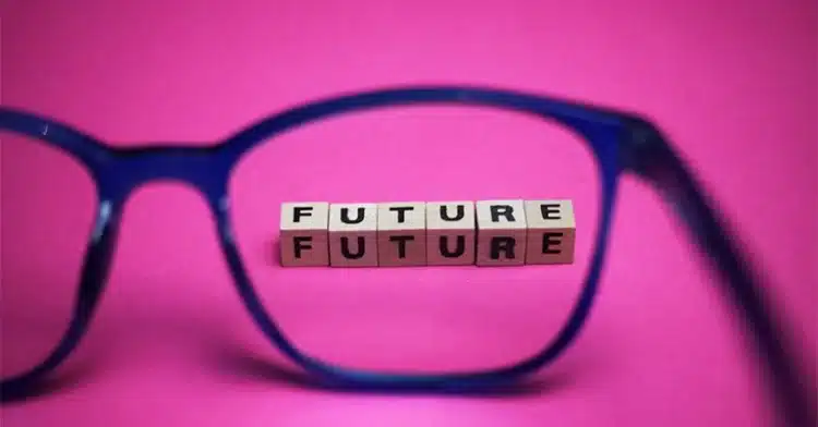 The word "FUTURE" spelled twice with wooden blocks, seen through a pair of glasses on a pink background.