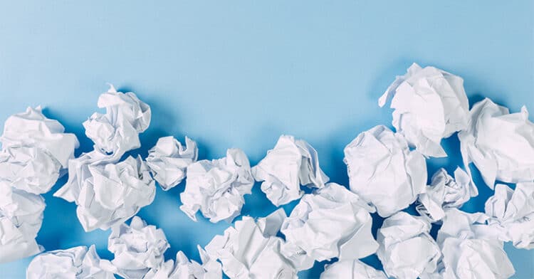 Crumpled paper balls scattered on a light blue surface, symbolizing failed ideas or creative frustration.
