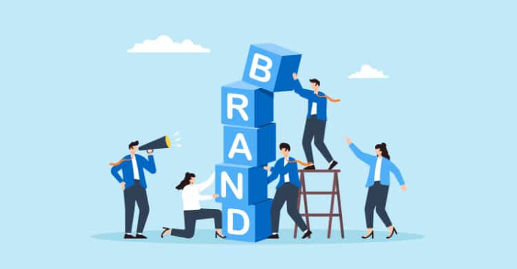 Undergrad Branding: How to Stand Out from the Crowd 5 Group of people stacking large blocks labeled "B" "R" "A" "N" "D" while collaborating and pointing upward. This visual represents undergrad branding by showing teamwork in building a strong and recognizable brand identity.