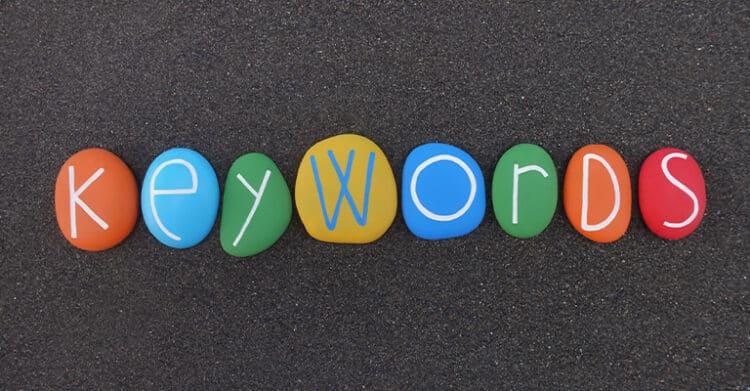 Colorful painted stones arranged in a row spell the word keywords against a dark textured background. The image visually represents keyword focus, search terms, or SEO concepts in a simple and playful way.
