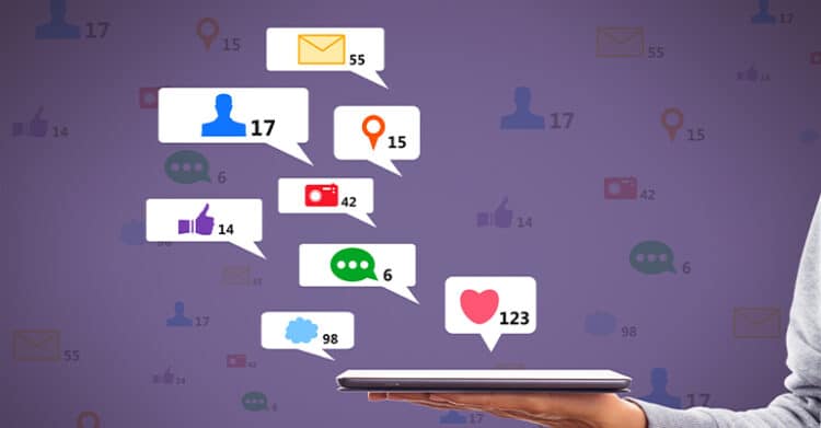 A hand holds a tablet with colorful notification icons floating above it, including messages likes comments photos and location pins with numbered counts. The image represents social media engagement, digital interaction, and tracking audience activity across online platforms.