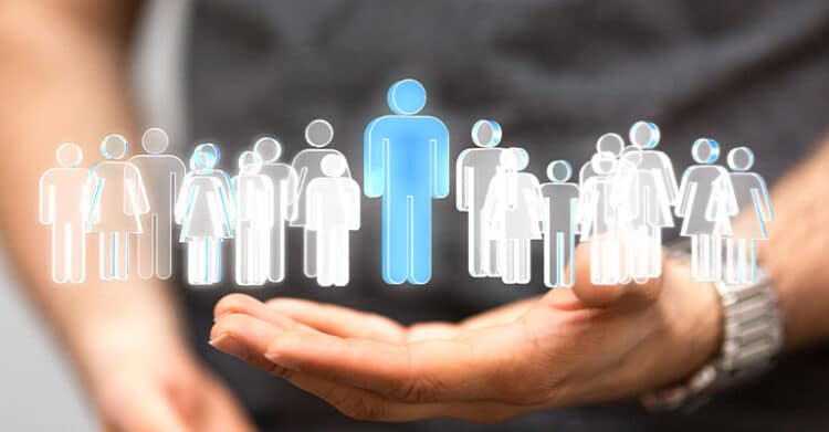 A hand is held open beneath a row of outlined human figures, with one larger blue figure highlighted at the center while the others appear in white and gray. The image connects to digital strategy by suggesting audience segmentation, customer targeting, or identifying a key user group.