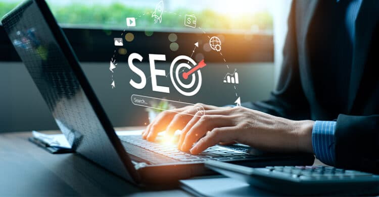 Hands type on a laptop keyboard while the word "SEO" appears in a digital overlay with a target in the letter O and small marketing icons around it. The image supports digital strategy by showing search optimization, online visibility, and performance focused digital marketing work.