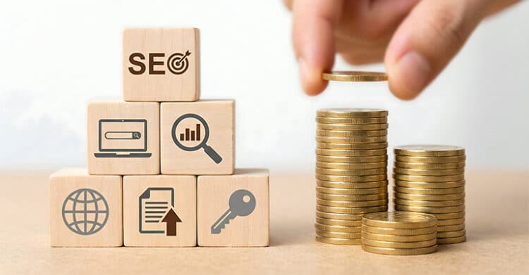 Wooden blocks stacked with SEO related icons beside rising stacks of gold coins as a hand places another coin on top. This visual suggests SEO strategy as a long term investment tied to search visibility, analytics, content, and business growth.