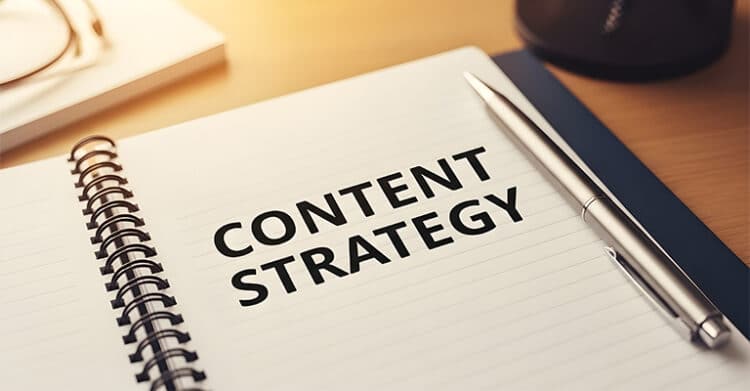 An open notebook with the words "CONTENT STRATEGY" printed in large bold letters beside a silver pen on a desk. This image connects content planning to SEO strategy by emphasizing the role of organized content in improving search visibility.
