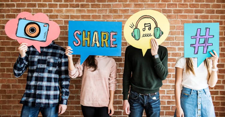 How to Build a Social Media Strategy That Works 5 Four people stand against a brick wall holding colorful speech bubbles with icons of a camera, the word "SHARE," headphones with music notes, and a hashtag symbol. This visual represents a social media strategy by highlighting content creation, sharing, and platform engagement.