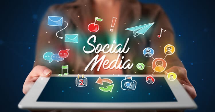 Person holding a tablet with the words Social Media glowing on the screen. Colorful icons float above it including email chat bubbles music notes a paper airplane camera calendar and network nodes to represent sharing content and engagement.