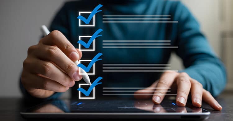 A person uses a stylus to check off a digital checklist with four blue check marks over a tablet screen. This image supports content marketing strategies by suggesting planning, review, and task management during content execution.