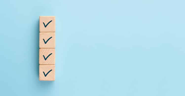 Four wooden blocks with check marks are stacked in a vertical row against a light blue background. This simple graphic represents an SEO strategy checklist or a series of completed optimization tasks.