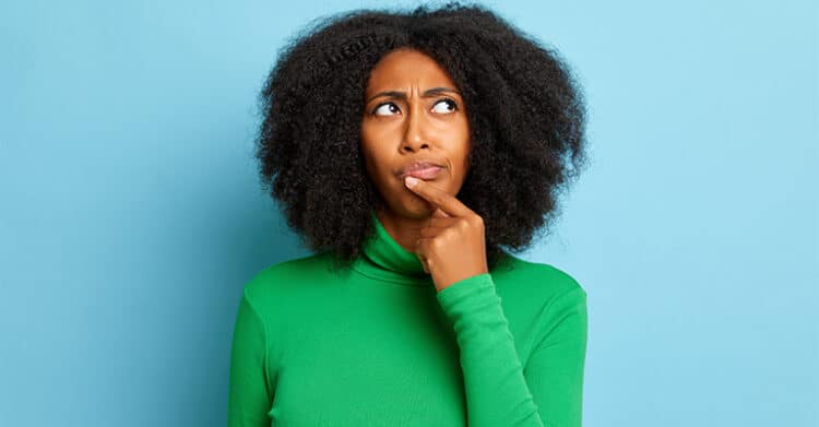 Woman in a bright green turtleneck looks up with a thoughtful expression and one finger resting on her lips against a light blue background. This portrait can support content about how to increase social media engagement by suggesting curiosity, strategy, and decision making.