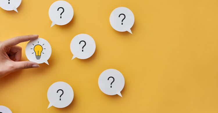 Hand holding a speech bubble with a light bulb icon among several speech bubbles marked with question marks on a yellow background. This graphic represents technical SEO by suggesting problem solving, troubleshooting, and finding answers to website performance issues.