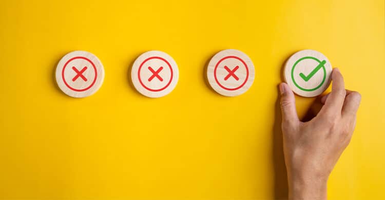 Hand placing a green checkmark wooden disc among three red X discs on a yellow background, representing social media marketing best practices and avoiding common mistakes.