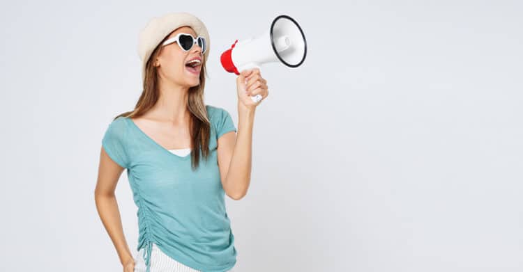 Woman wearing sunglasses and a hat holding a megaphone and shouting while facing sideways against a plain background. Visual representation of social media rules highlighting broadcasting messages and speaking to an online audience.
